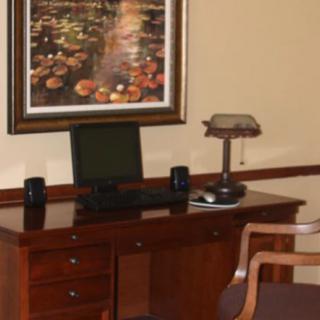 A tidy office desk setup with a computer, lamp, and decorative painting.
