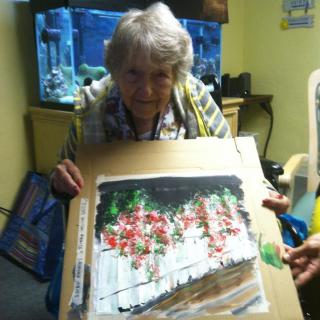 An elderly woman proudly displaying her painting next to an aquarium.