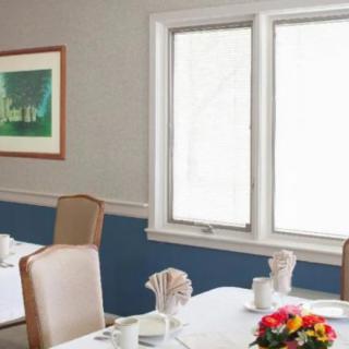 A cozy dining room with tables set for a meal, featuring bright flowers and framed art on the wall.