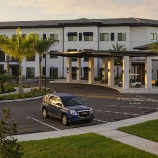 A modern building with a car parked in front, surrounded by palm trees under a clear sky.