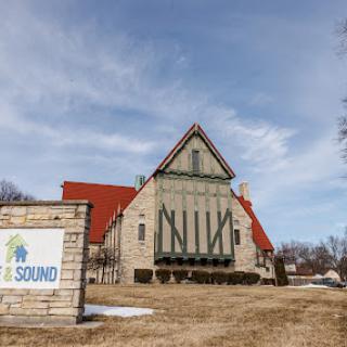 A unique architectural structure with a red roof and green shutters, accompanied by a sign in front.