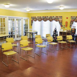 An empty classroom with yellow chairs arranged in rows on a wooden floor.