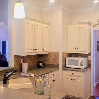 A modern kitchen with cream-colored cabinets and a countertop featuring a microwave and a pitcher of lemon water.