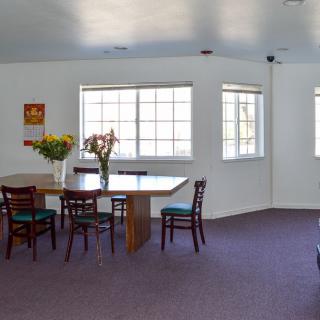 A simple dining area with a table, chairs, and flowers near large windows.