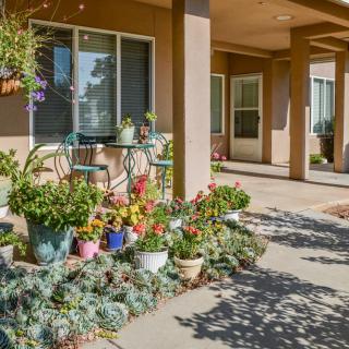 A cozy patio area featuring colorful flowers and potted plants, complete with a table and chairs for outdoor relaxation.