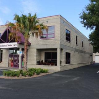 A commercial building with a palm tree in front and an adjacent parking area on a clear day.