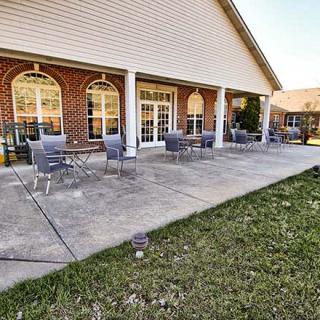 A patio area with chairs and tables outside a brick building with large windows.