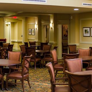 A spacious dining area with multiple tables and chairs, softly lit with wall-mounted lamps and decorated with framed artwork.