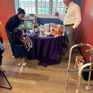 A gathering featuring a table with various items, where adults and a child interact.