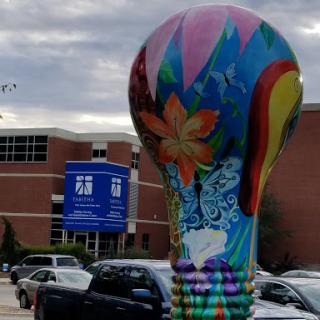 A vibrant, artistic light bulb sculpture stands out in front of a building.