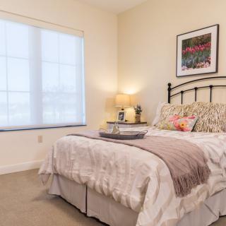 A cozy bedroom with a neatly made bed, soft lighting, and a window providing natural light.