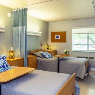 A hospital room with two beds separated by a curtain, featuring lamps and a window.