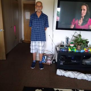 A person standing in a living room with casual attire, next to a television displaying a show.