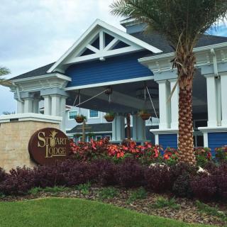 A beautifully landscaped entrance to a blue and white building with palm trees and vibrant flowers.