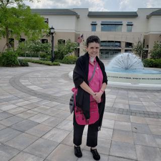 A woman standing near a fountain in an outdoor setting.
