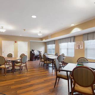 A spacious dining area with multiple tables and chairs set on a hardwood floor, featuring large windows and ceiling lights.