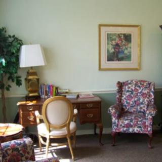 A cozy living room corner with a floral armchair, desk, and lamp.