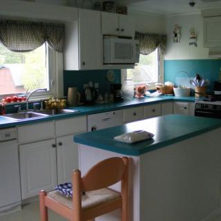 A cozy kitchen with teal countertops, white cabinets, and natural light from two windows.