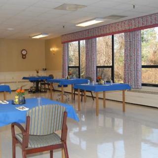 A well-lit dining room with tables covered in blue tablecloths and large windows along one wall.