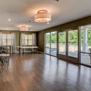 A spacious dining room with wood flooring, large windows, and elegant chandeliers.