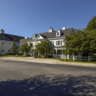 A picturesque view of a residential building with trees lining the road under a clear blue sky.