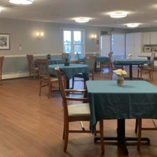 An empty dining room with neatly arranged tables and chairs, featuring wooden floors and soft lighting.