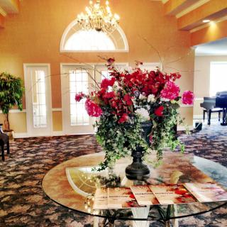 A beautifully decorated lobby featuring a grand flower arrangement, elegant chandelier, and a grand piano.