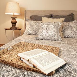 A cozy bedroom setting with a book open on a tray, surrounded by patterned pillows and a warm lamp.