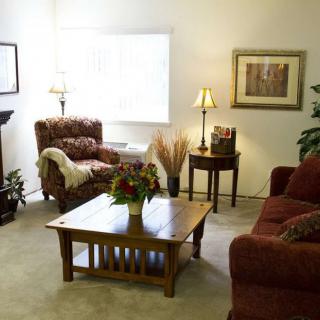 A cozy living room with a sofa, armchair, and coffee table, decorated with plants and artwork.
