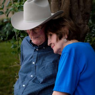 An elderly couple sharing a tender moment outdoors, with the man wearing a cowboy hat.