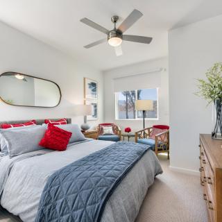 A modern and cozy bedroom with a stylish design, featuring a comfortable bed, decorative pillows, a ceiling fan, and plenty of natural light.