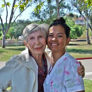 An elderly woman and a younger woman smiling together in a park.