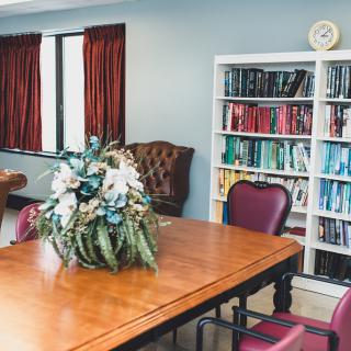 A cozy conference room with a wooden table, bookshelf, and floral centerpiece.