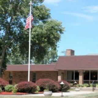 A single-story brick building with an American flag and surrounding greenery.
