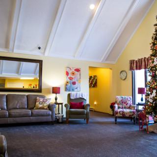 A cozy living room decorated for the holidays with a Christmas tree, sofa, and armchairs.