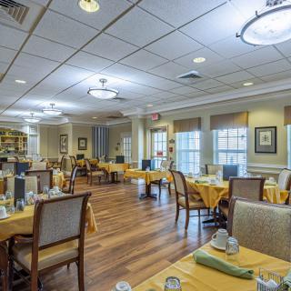 An elegant dining room with neatly arranged tables and chairs, featuring large windows and chandeliers.