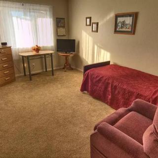 A cozy, carpeted bedroom with natural light and simple furniture.