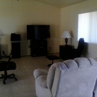A cozy living room with a television, sofa, chairs, and a lamp.
