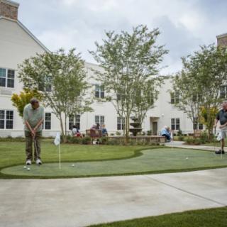 People enjoying a game of golf on a putting green in front of a building.