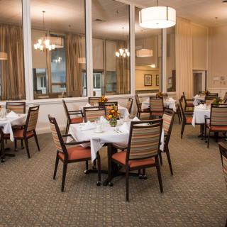 An elegant dining area with neatly arranged tables and chairs, featuring soft lighting and large windows.