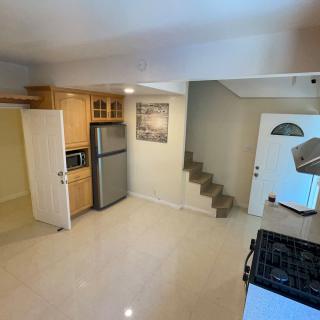 A modern kitchen with wooden cabinets, appliances including a fridge and microwave, and an adjacent staircase.