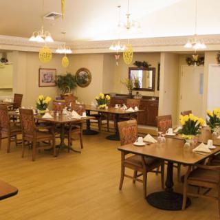 A well-lit dining room interior with neatly arranged tables and chairs, adorned with decorative plants.
