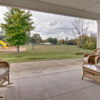 A cozy patio with wicker chairs overlooks a lush lawn and playground.