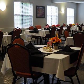 An elegantly set dining room with multiple tables and chairs, each adorned with flowers and dark napkins.