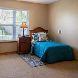 A cozy bedroom with a single bed, nightstand, and a window letting in natural light.