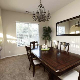 A well-lit dining room featuring a wooden table with matching chairs, a decorative chandelier, and a large mirror.