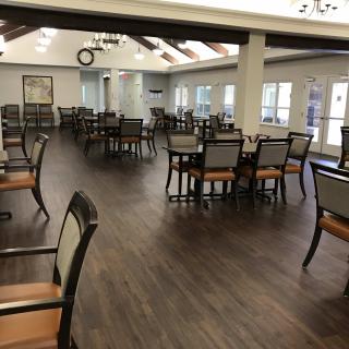 An empty dining room with wooden floors and neatly arranged tables and chairs.