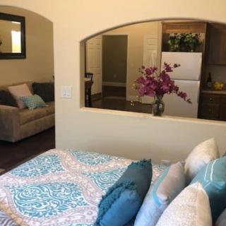 A cozy open-plan living space featuring a bedroom with a patterned quilt and colorful pillows, connected to a living area with a sofa and floral arrangement.