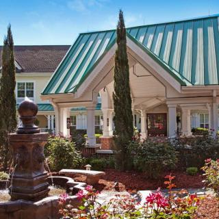 A beautifully landscaped entrance featuring a fountain and garden in front of a building with a green metal roof.