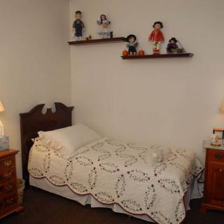 A cozy bedroom with a vintage quilt on the bed and shelves displaying decorative dolls.